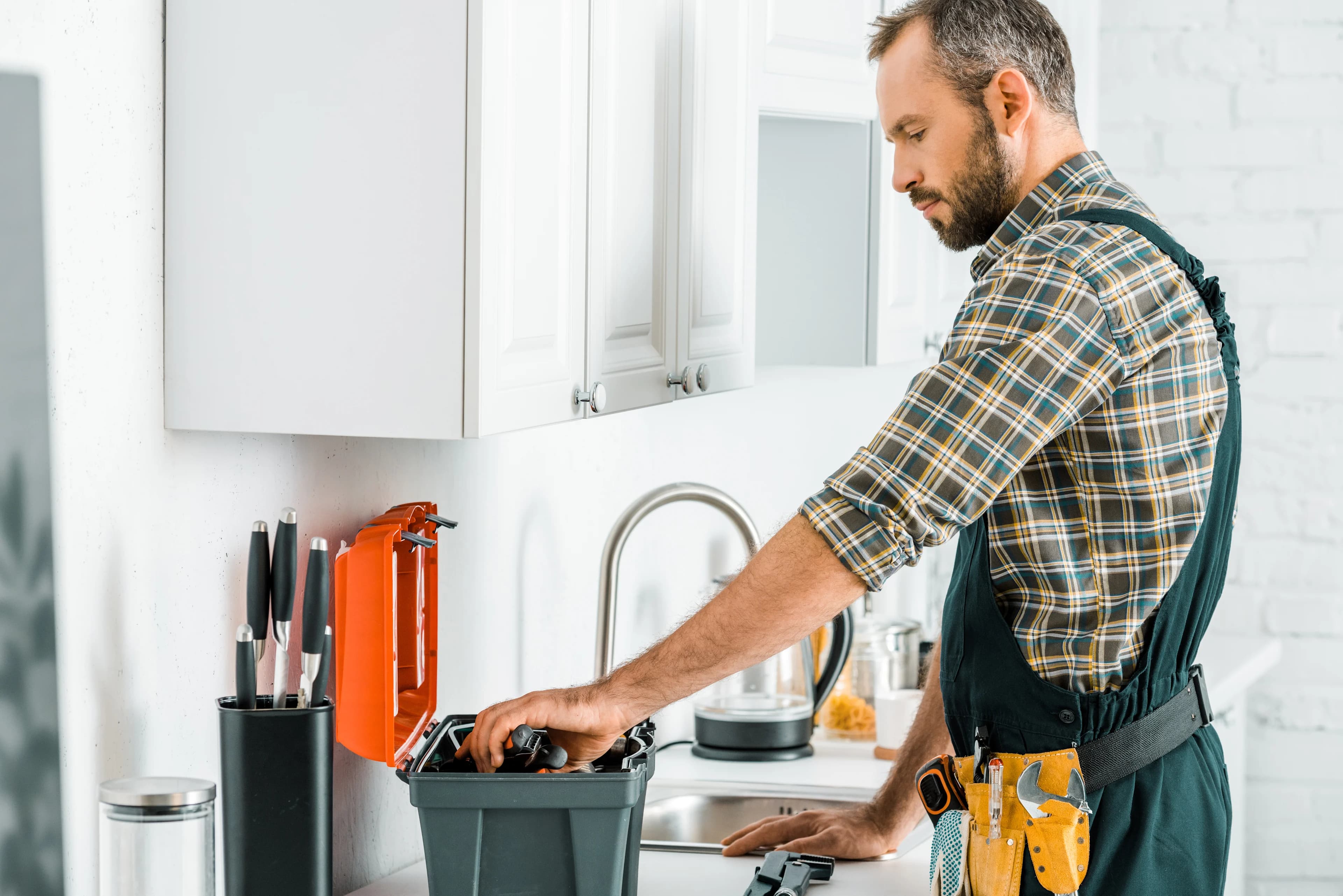 Profissional autônomo com cinto de ferramentas organizando uma caixa de ferramentas em uma cozinha